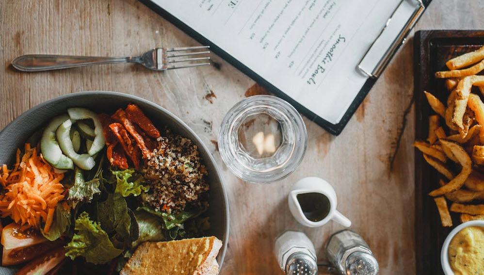 Downward looking image of a dinning table with a couple plates of food, condiments, a fork and a clipboard type of menu.  No links in this image